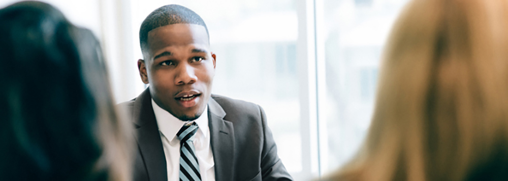 Photo of a black man in front of two persons talking